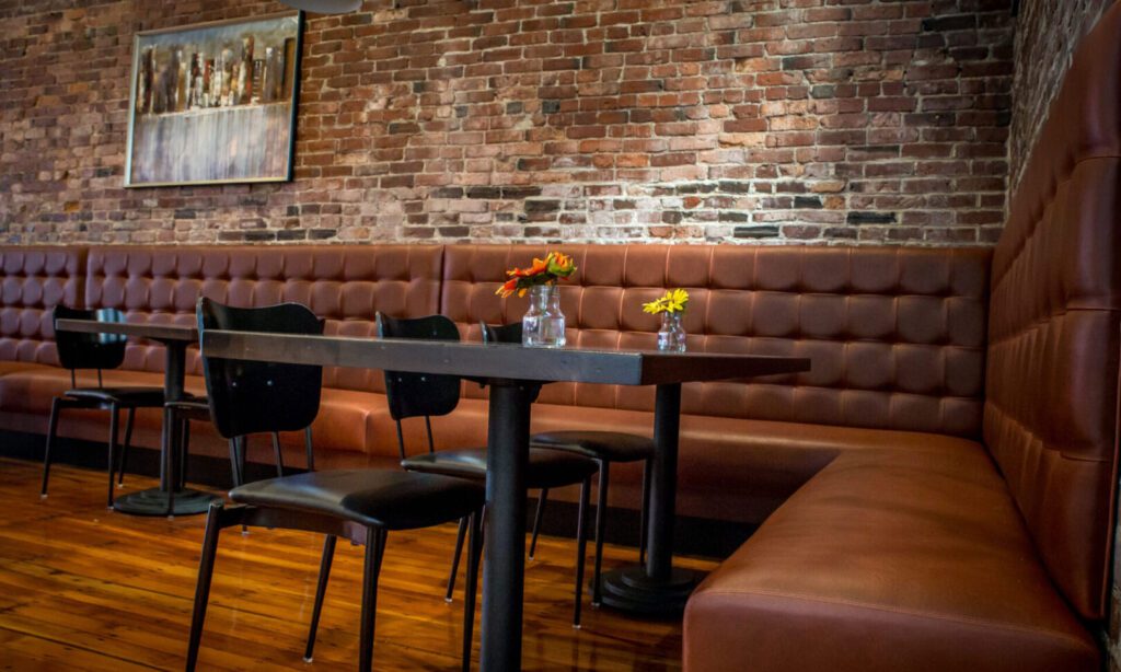 Cozy restaurant seating with tufted leather bench and black chairs.